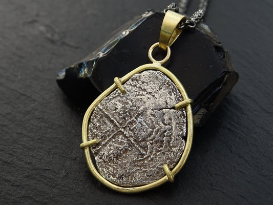 Atocha 2 Reales coin pendant set in 18k gold with black sterling silver chain on dark background