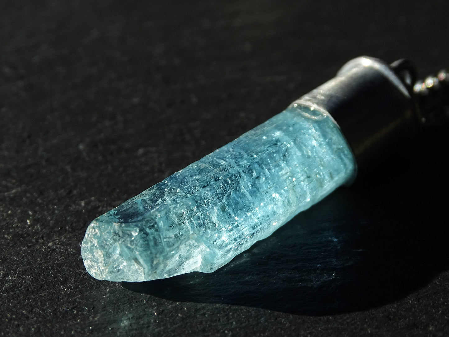 Close-up of raw aquamarine crystal pendant set in black sterling silver with natural blue hues and textured surface