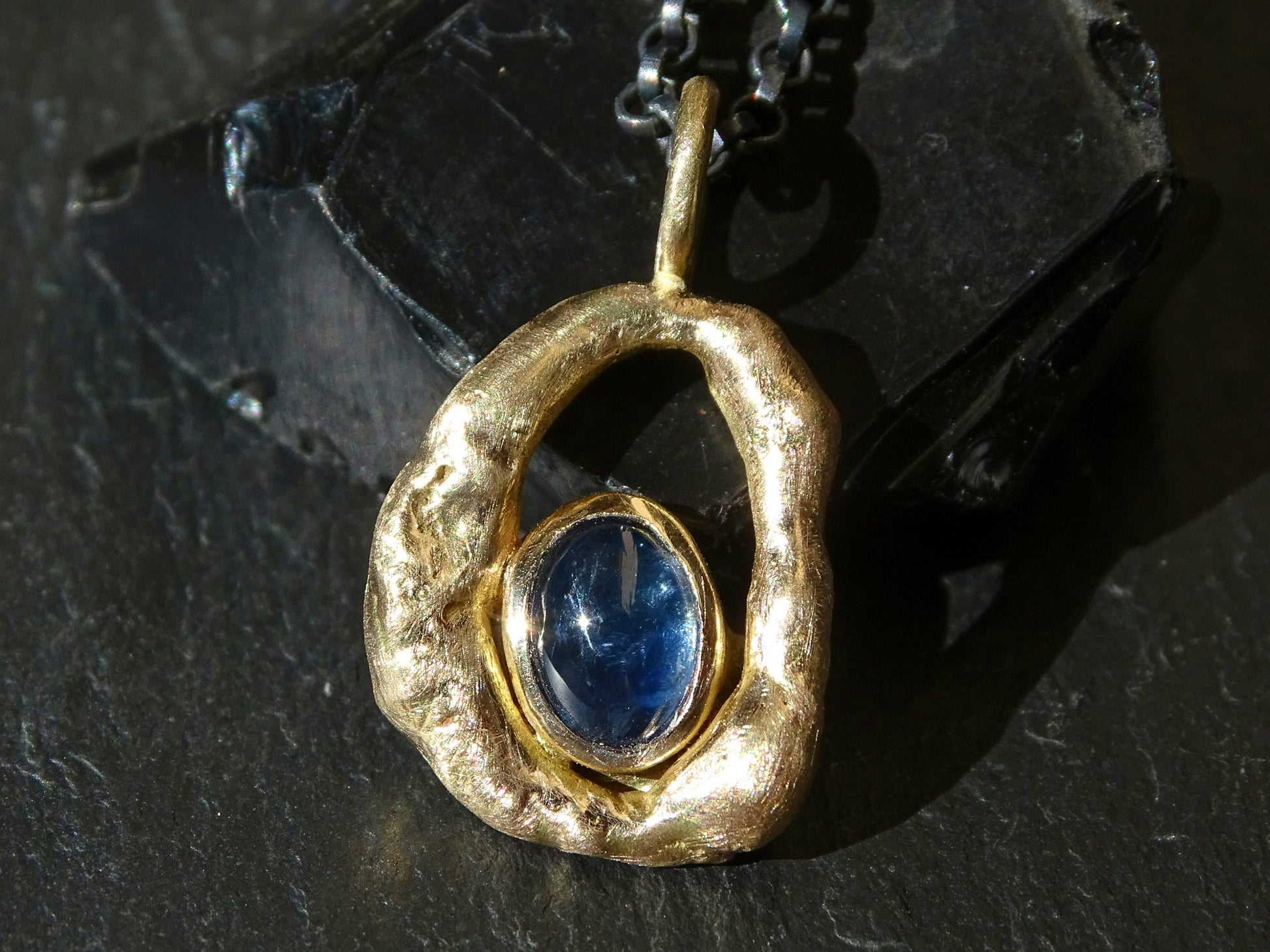 blue sapphire pendant with oval cabochon sapphire set in organic molten 14k gold frame on black sterling silver chain