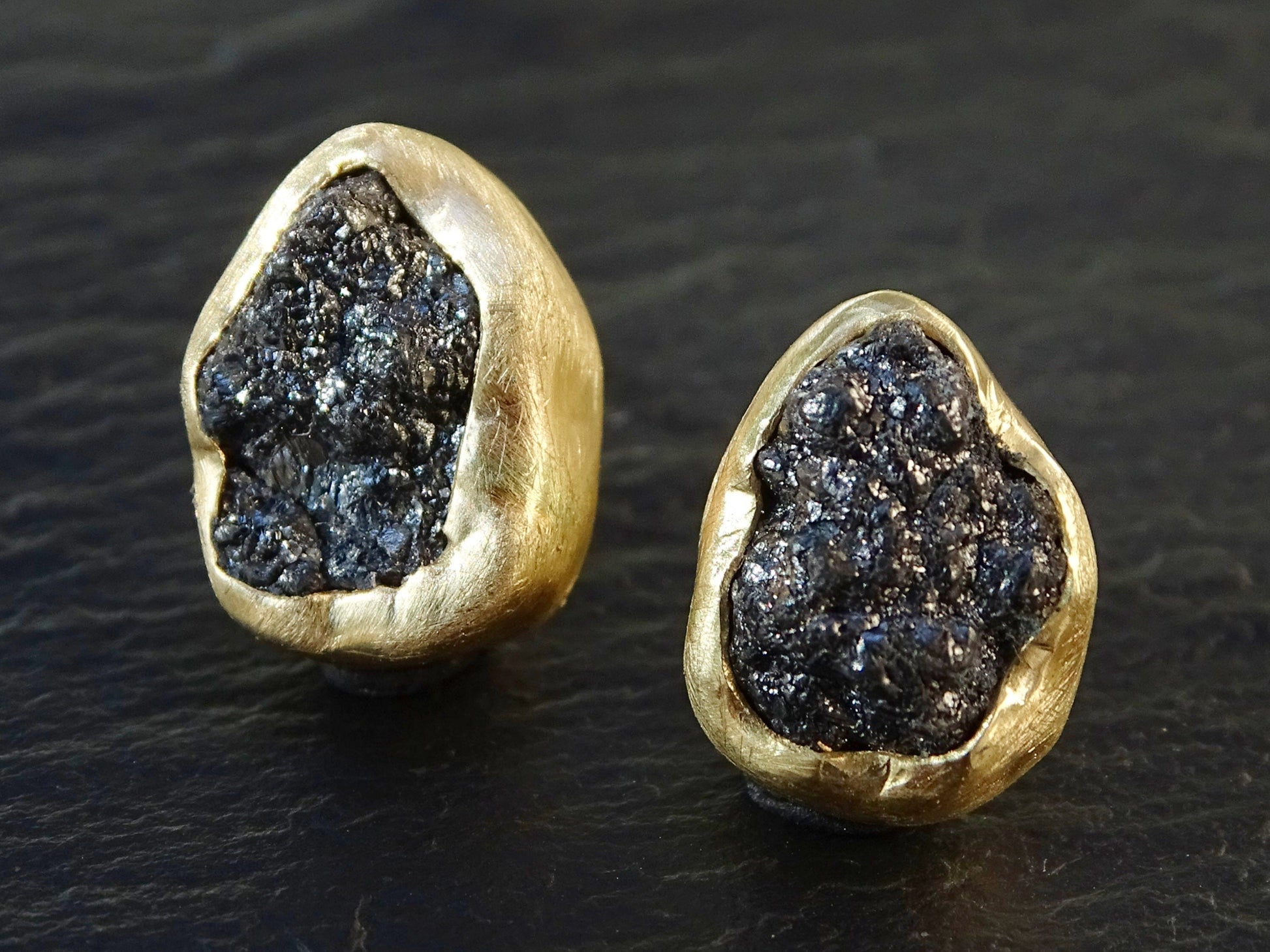 Raw black diamond stud earrings set in 14k yellow gold bezel settings.