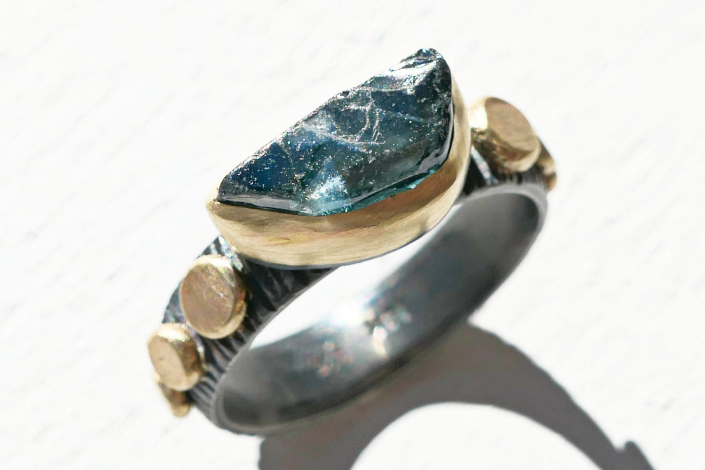 Blue sapphire engagement ring with uncut teal-blue gemstone in 14k gold bezel and black oxidized silver band size 7 1/4