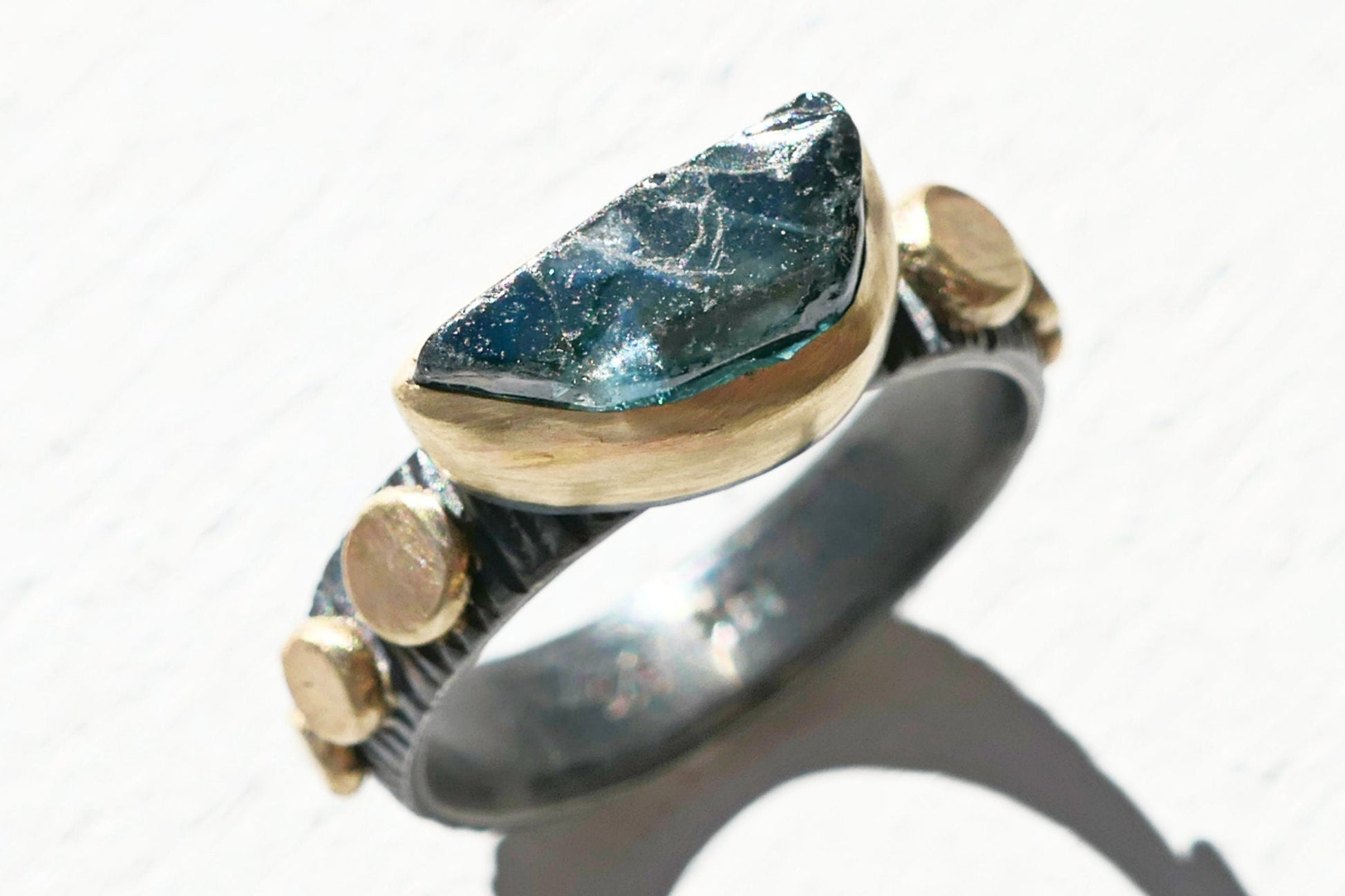 Blue sapphire engagement ring with uncut teal-blue gemstone in 14k gold bezel and black oxidized silver band size 7 1/4