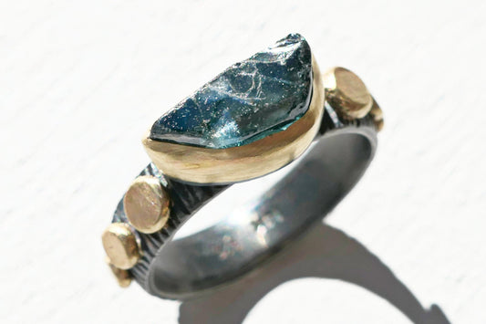Blue sapphire engagement ring with uncut teal-blue gemstone in 14k gold bezel and black oxidized silver band size 7 1/4