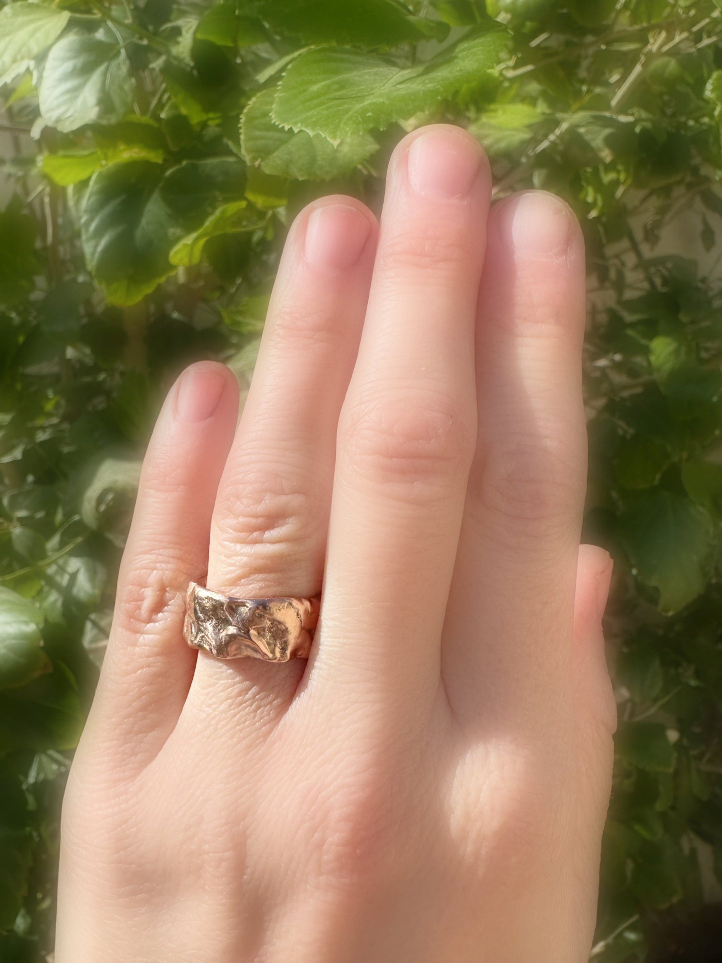 molten gold wedding ring on hand with green background