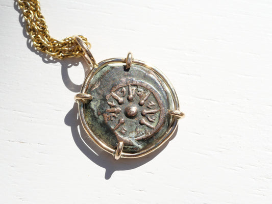Widows Mite coin pendant with a weathered green-brown patina, round bronze coin, and gold-tone prong setting with chain.