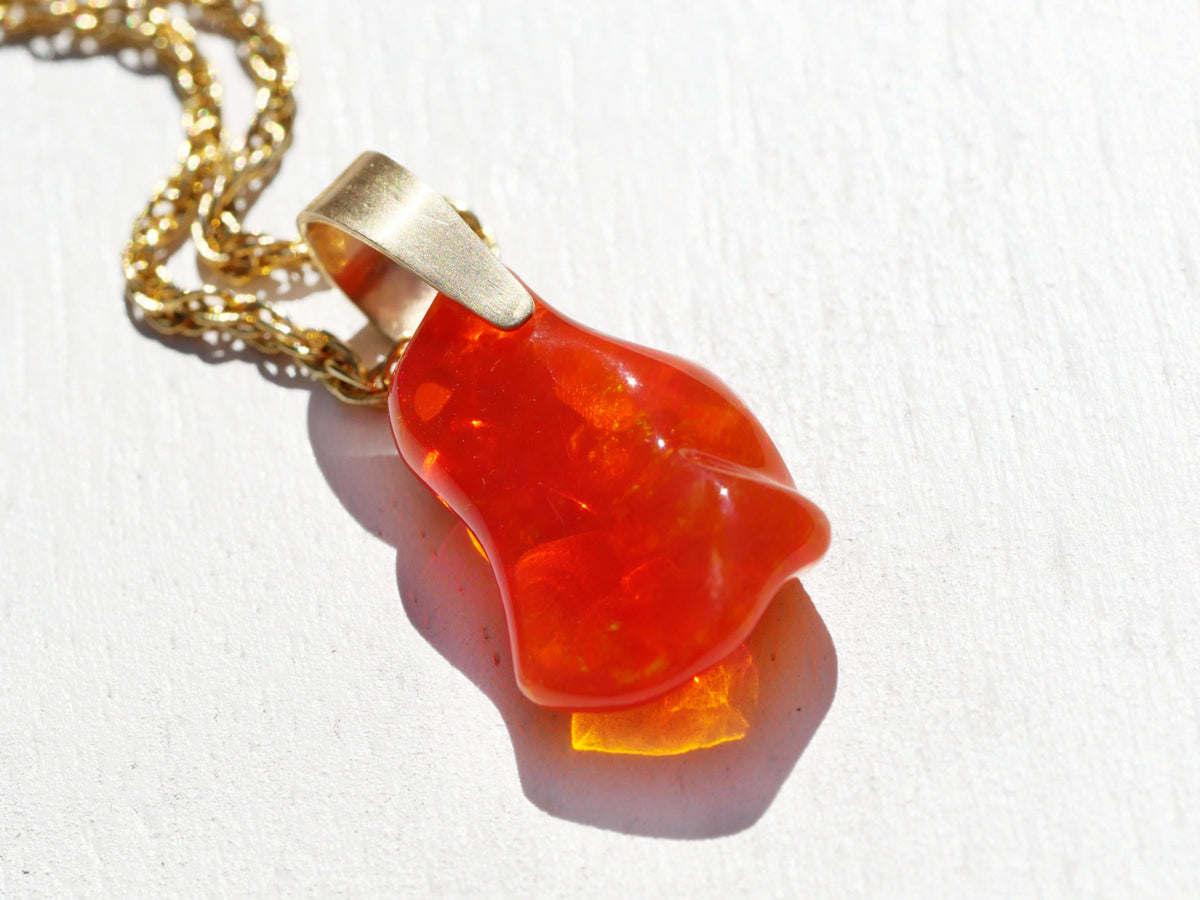 Carved Mexican Fire Opal Pendant in translucent red-orange stone, with an organic carved shape and gold-tone bail and chain.
