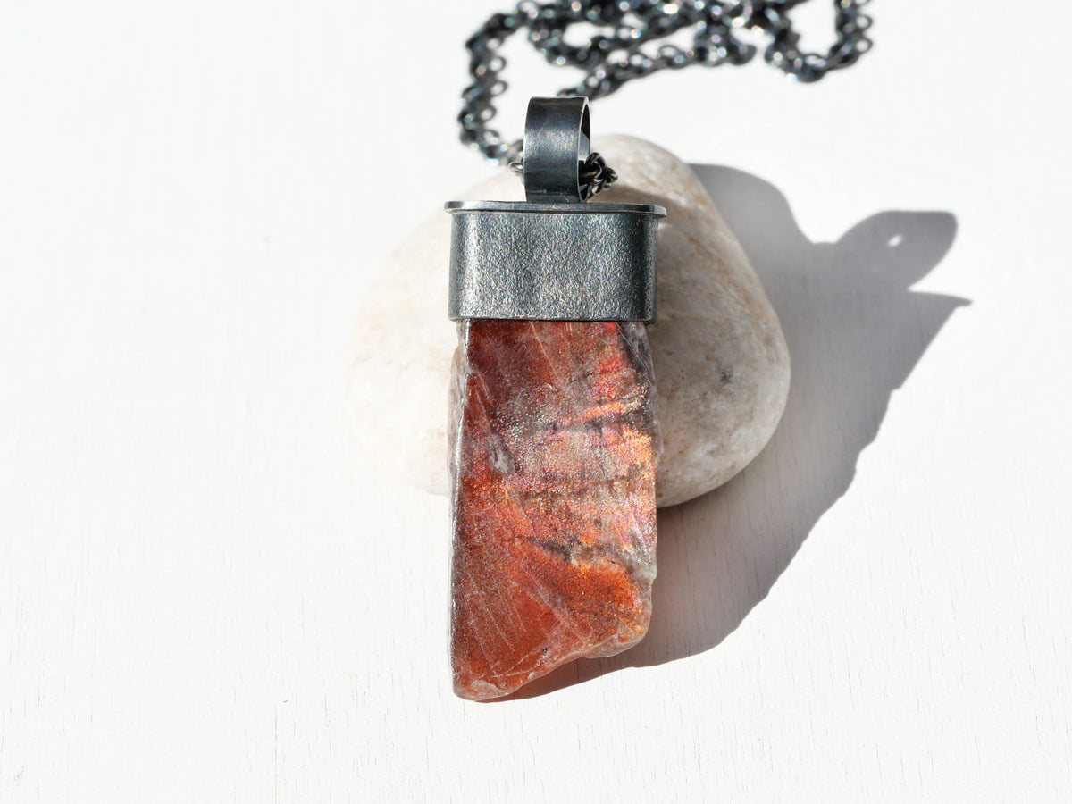 Raw Purple Haze Sunstone pendant in red-orange chatoyant crystal, set in textured dark oxidized sterling silver with chain