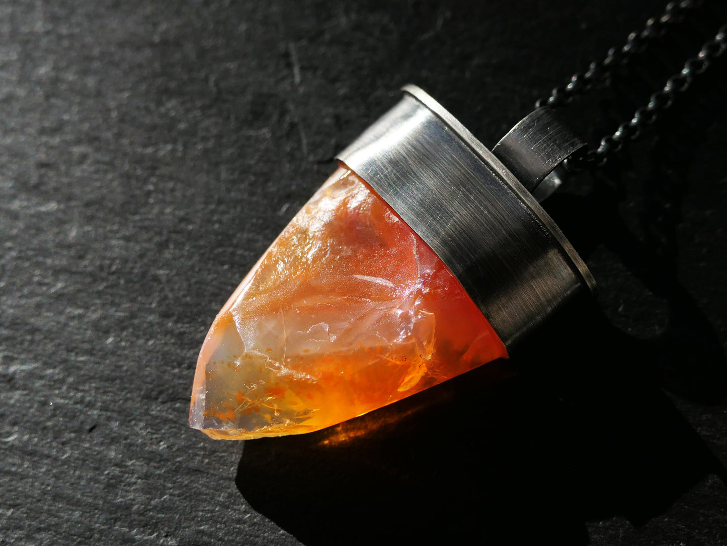 Partially cut orange fire opal pendant in handcrafted sterling silver setting with a dark chain.